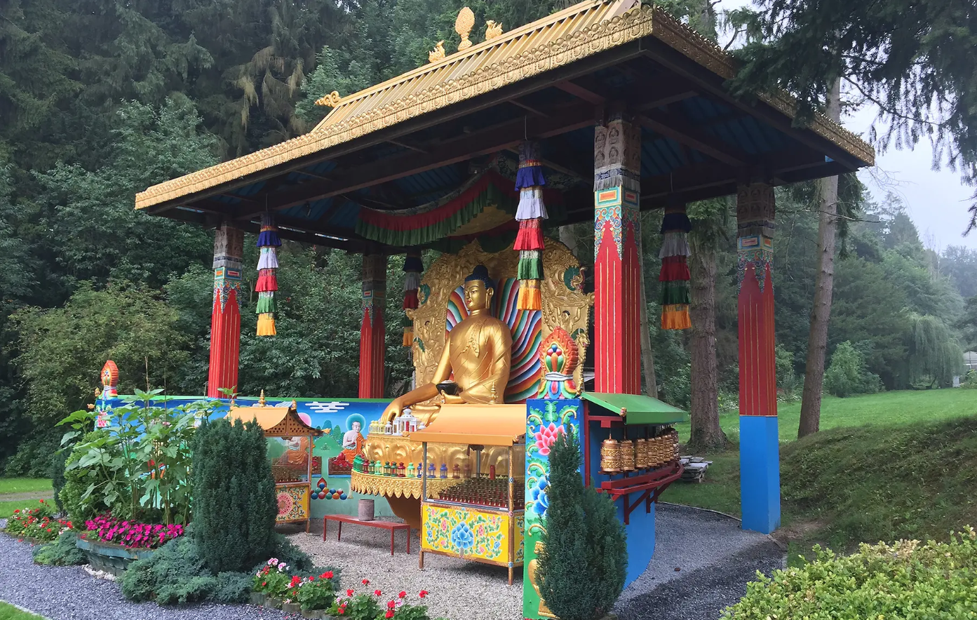 Colourful Tibetan Buddhist shrine with a gilded Buddha, set among trees and flower beds