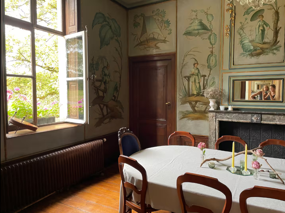 Corner of the dining room with an open window, muralled walls and a table laid with candles
