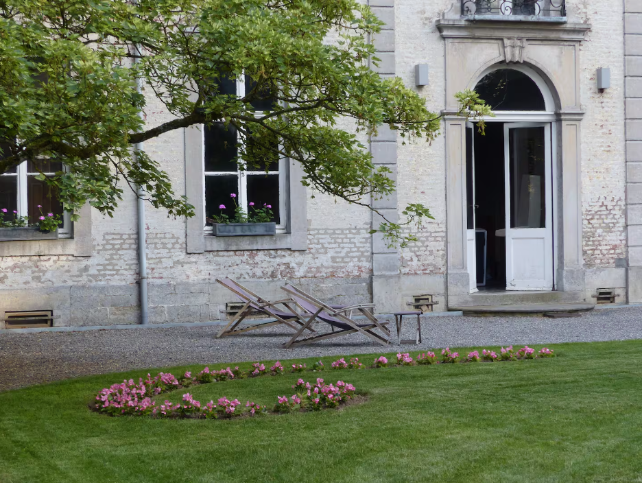 Weathered stone facade with an arched doorway, wooden deckchairs and a curving flower bed
