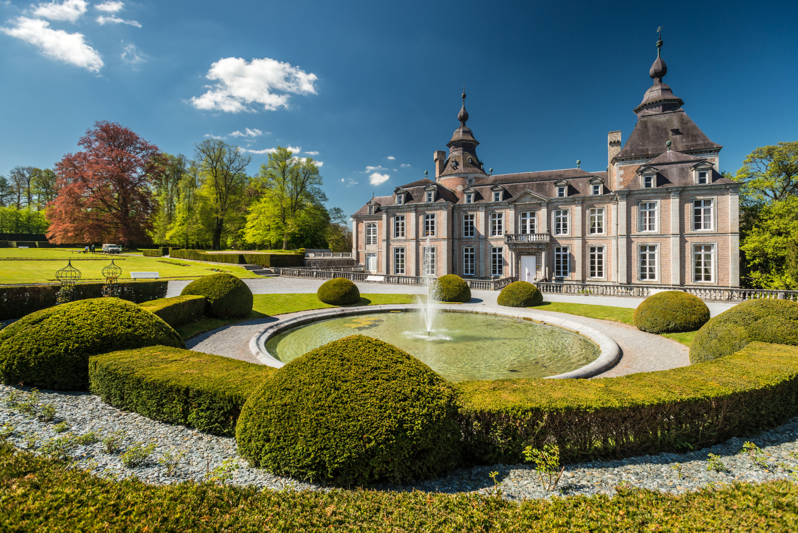 Château de Modave seen across its formal garden with clipped hedges and a fountain