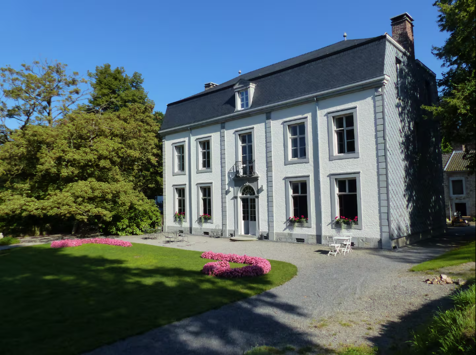 Pale grey eighteenth-century mansion with a slate roof, seen across a lawn with pink flower beds